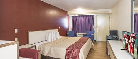 A hotel room with a bed, a desk, a television, and a door.