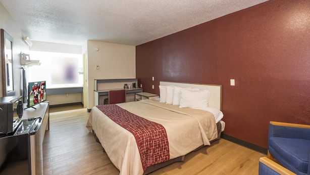 A hotel room with a bed, a desk, a chair, a TV, and a window.