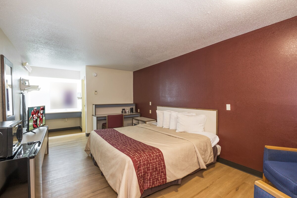 A hotel room with a bed, a desk, a chair, a TV, and a window.