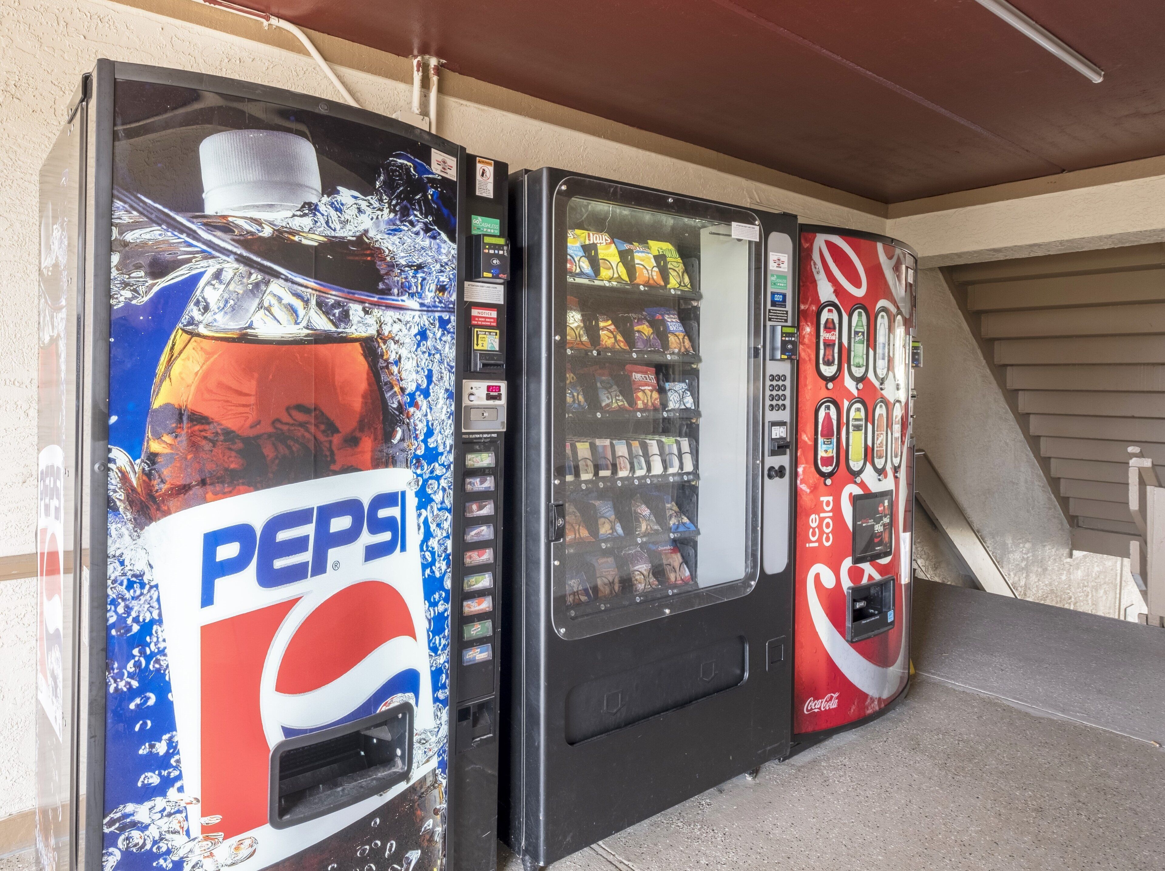 Three beverage vending machines, one with a Pepsi logo, another with a Coca-Cola logo, and a third with a variety of snacks.