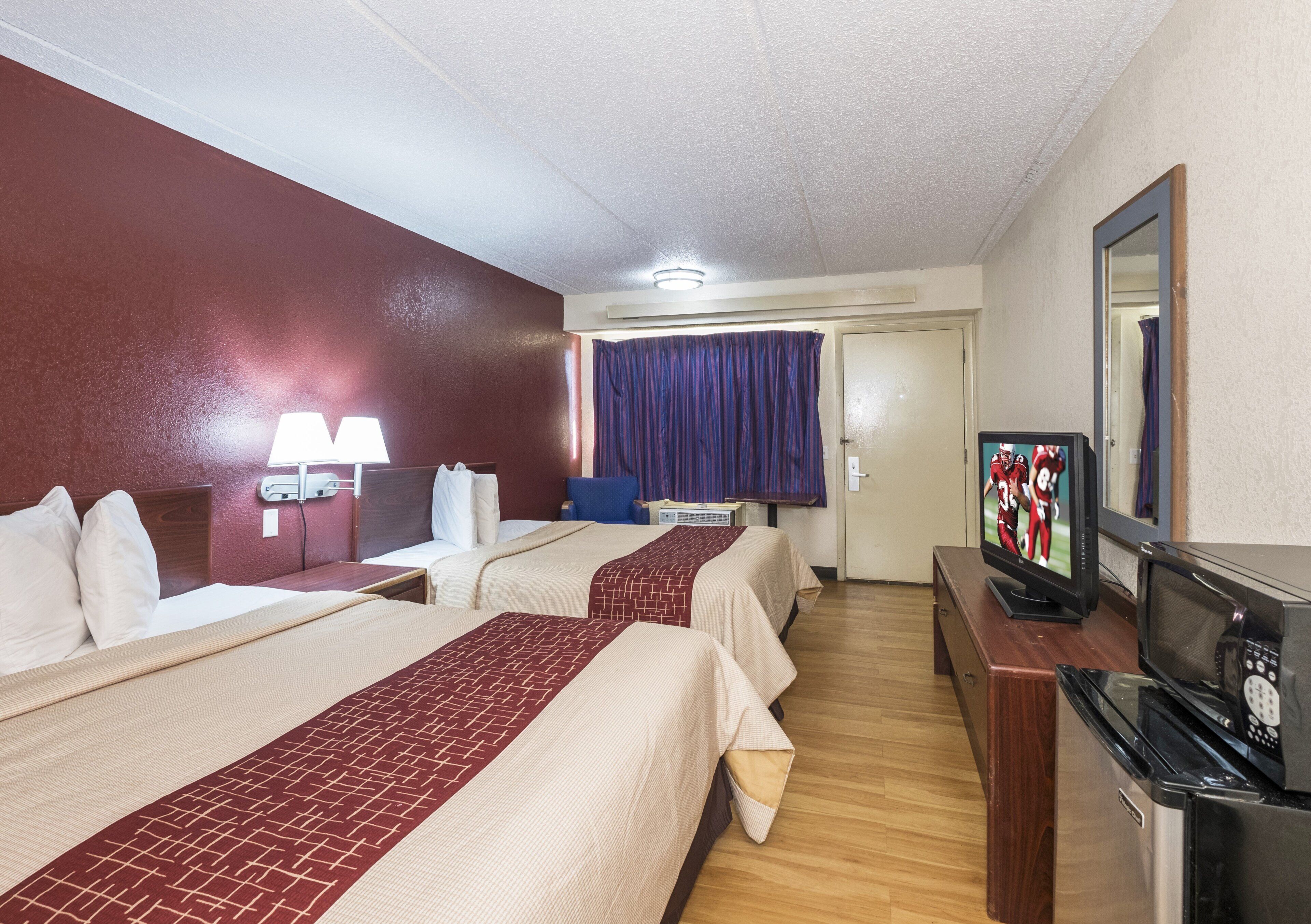 A hotel room with two beds, a television, a microwave, and a small desk.
