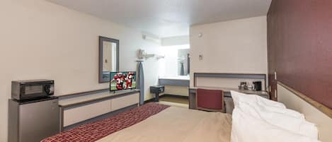Habitación de hotel con cama, escritorio, microondas, televisor y espejo.