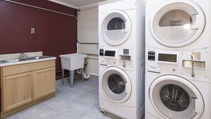 A laundry room with two stacked front-loading washing machines, a sink, and wooden cabinets.