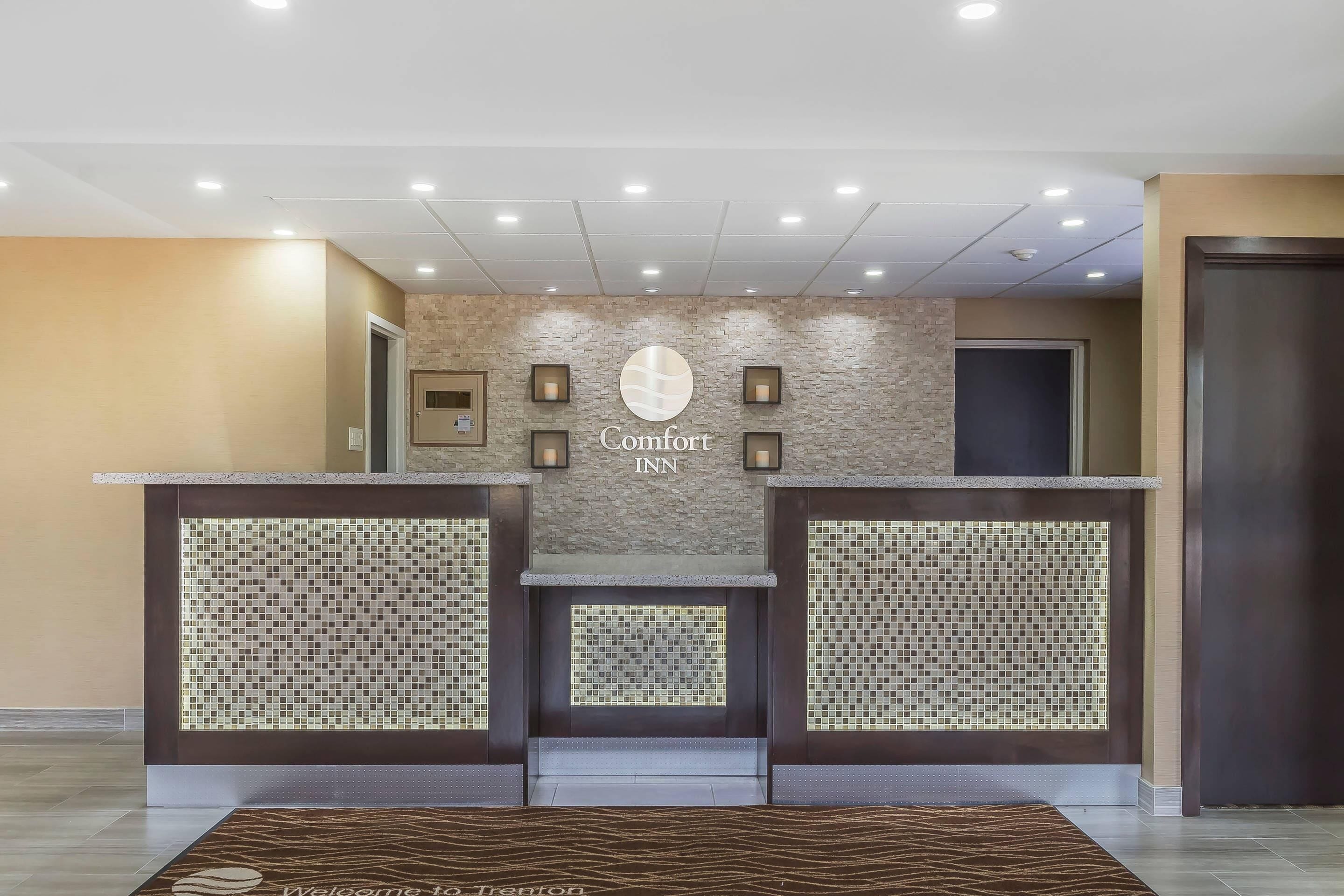 Una recepción con el letrero de 'Comfort Inn', un muro de mosaico de baldosas y una alfombra estampada.