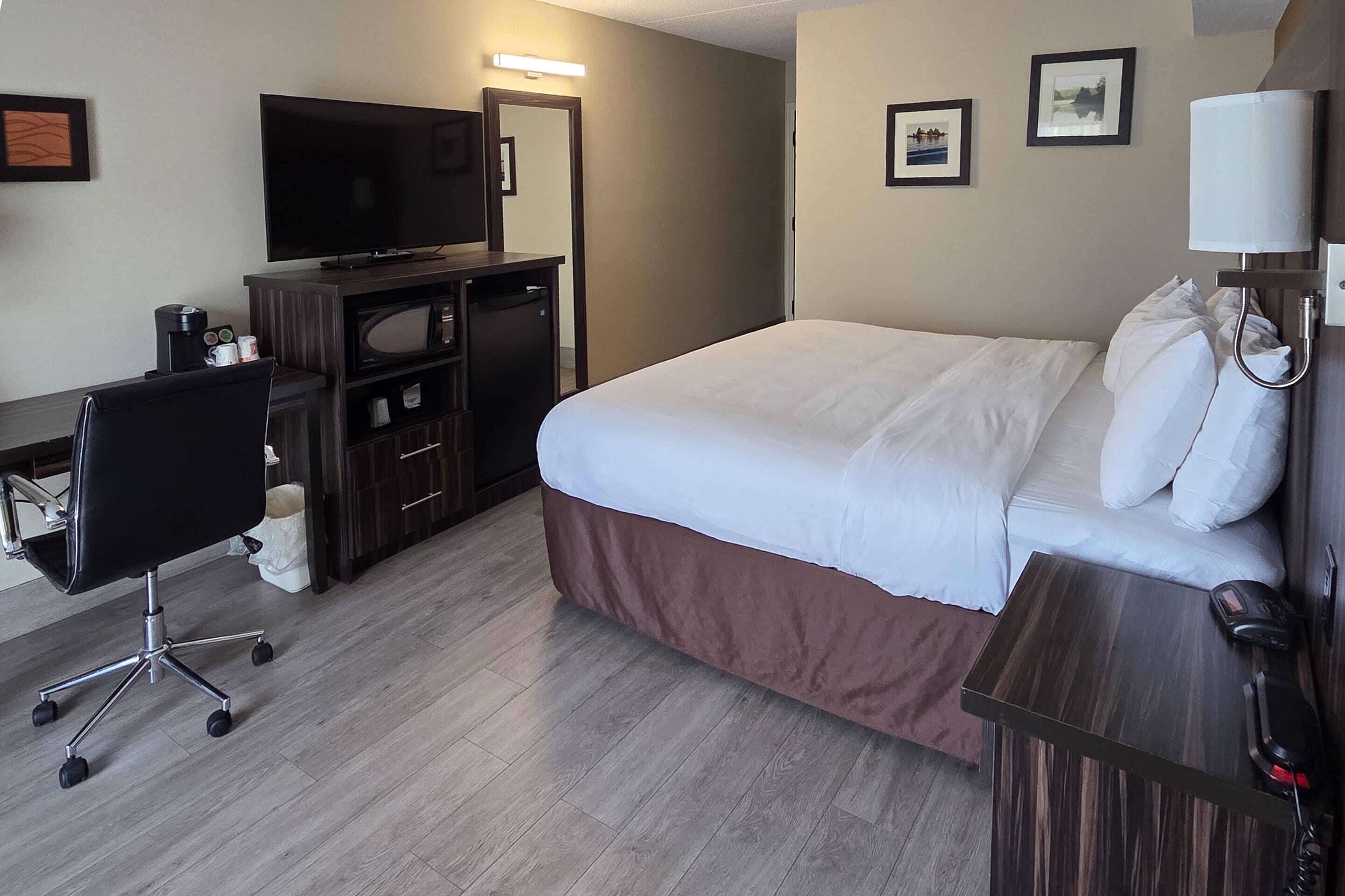 Een hotelkamer met een bed, een bureau met een computer, een stoel, een televisie en een lamp.
