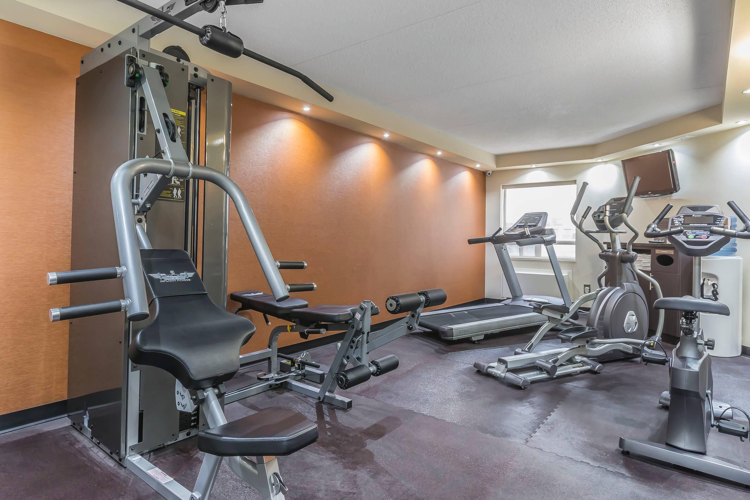 Un gimnasio con diversos equipos de ejercicio, incluyendo una prensa de banca, cintas de correr y una máquina elíptica.