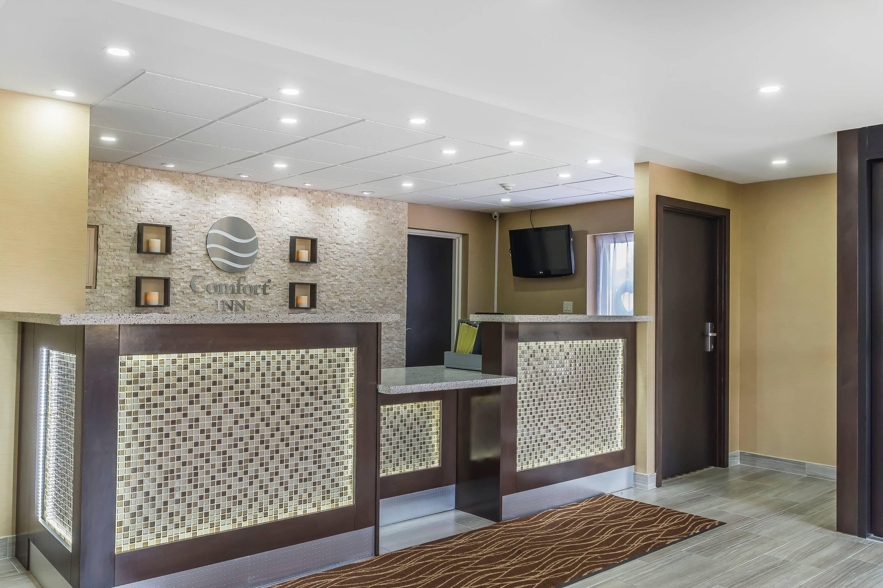 Zona de recepción de un hotel con pared de piedra, televisor montado en la pared y mostrador de recepción.