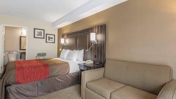 A hotel room with a bed, a sofa, a nightstand with a phone, and a wall-mounted light fixture.