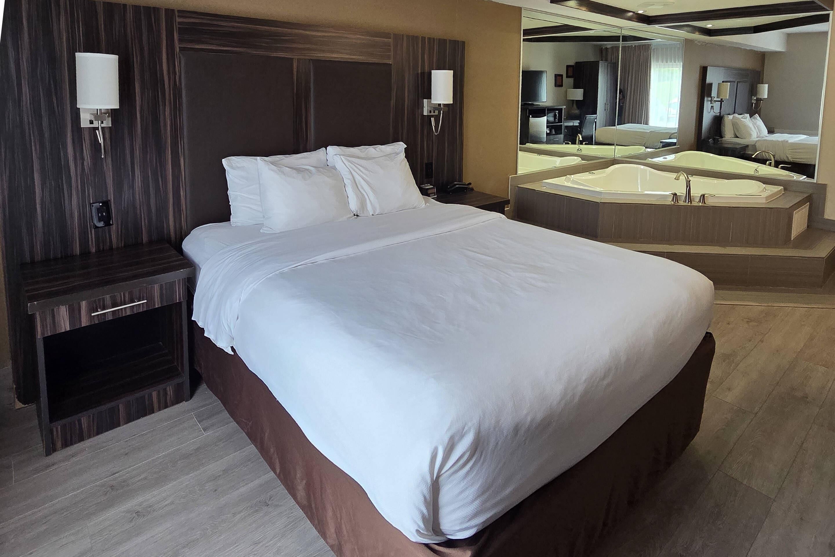 A hotel room with a large bed, a sitting area with a desk, a large mirror, and a bathtub.