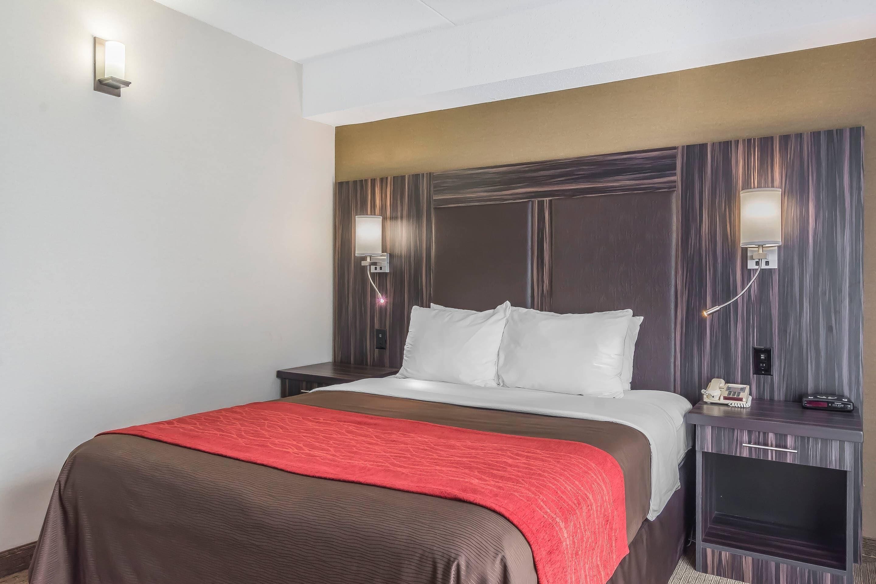 A hotel room with a bed, bedside tables, a nightstand, a wall-mounted lamp, and a telephone.