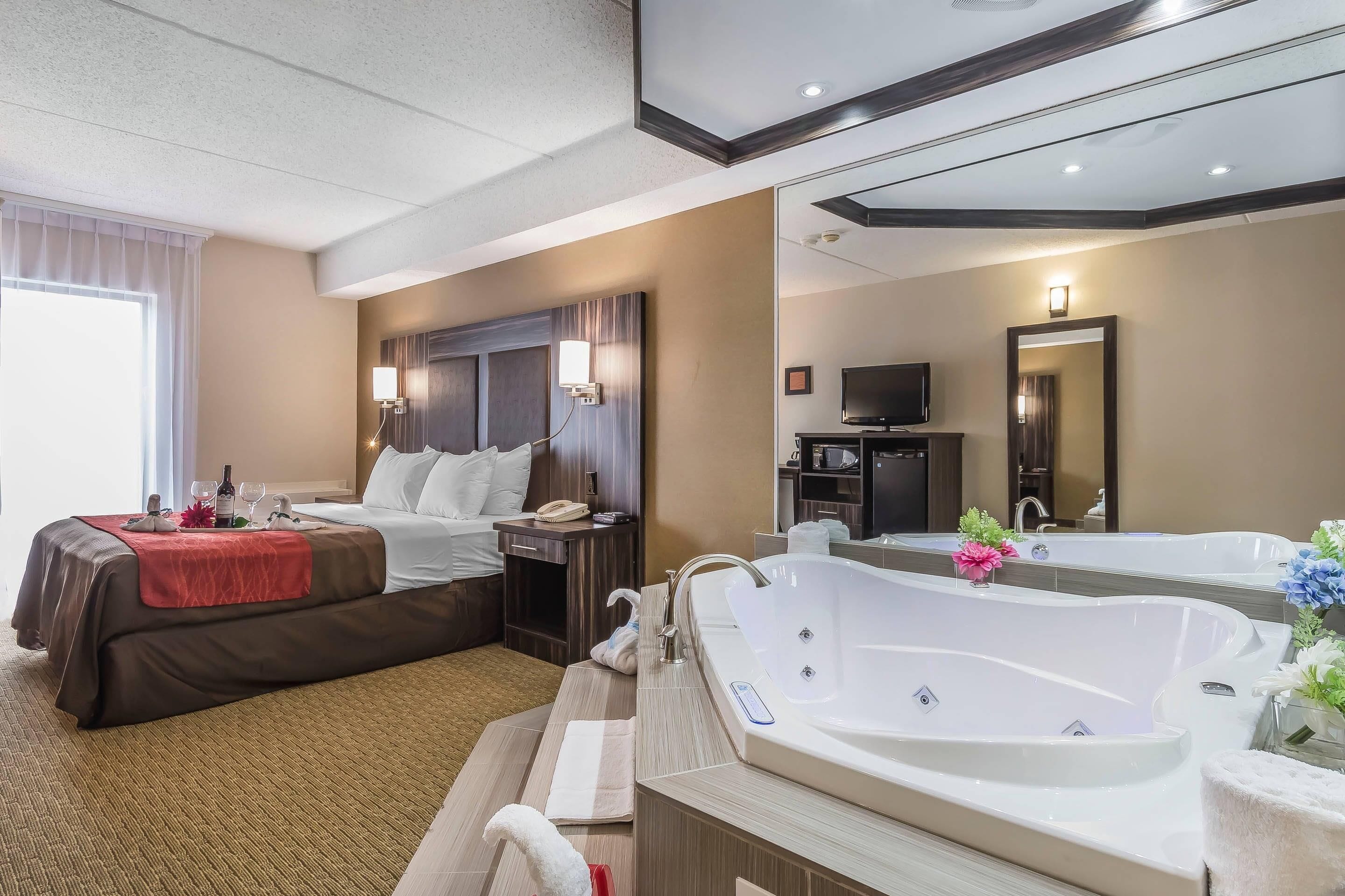 Ein Hotelzimmer mit einem Bett, einem Schreibtisch, einem Fernseher, einem Badezimmer mit Badewanne und einem großen Spiegel.