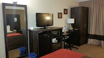 Habitación de hotel con cama, escritorio con computadora, televisión, espejo, armario y baño.