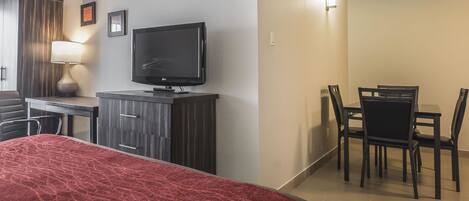 Habitación de hotel con cama, escritorio con televisor, mesa de comedor y sillas, y armario.