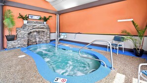 Une piscine intérieure avec un mur en pierre, des plantes en pot et un sol bleu.