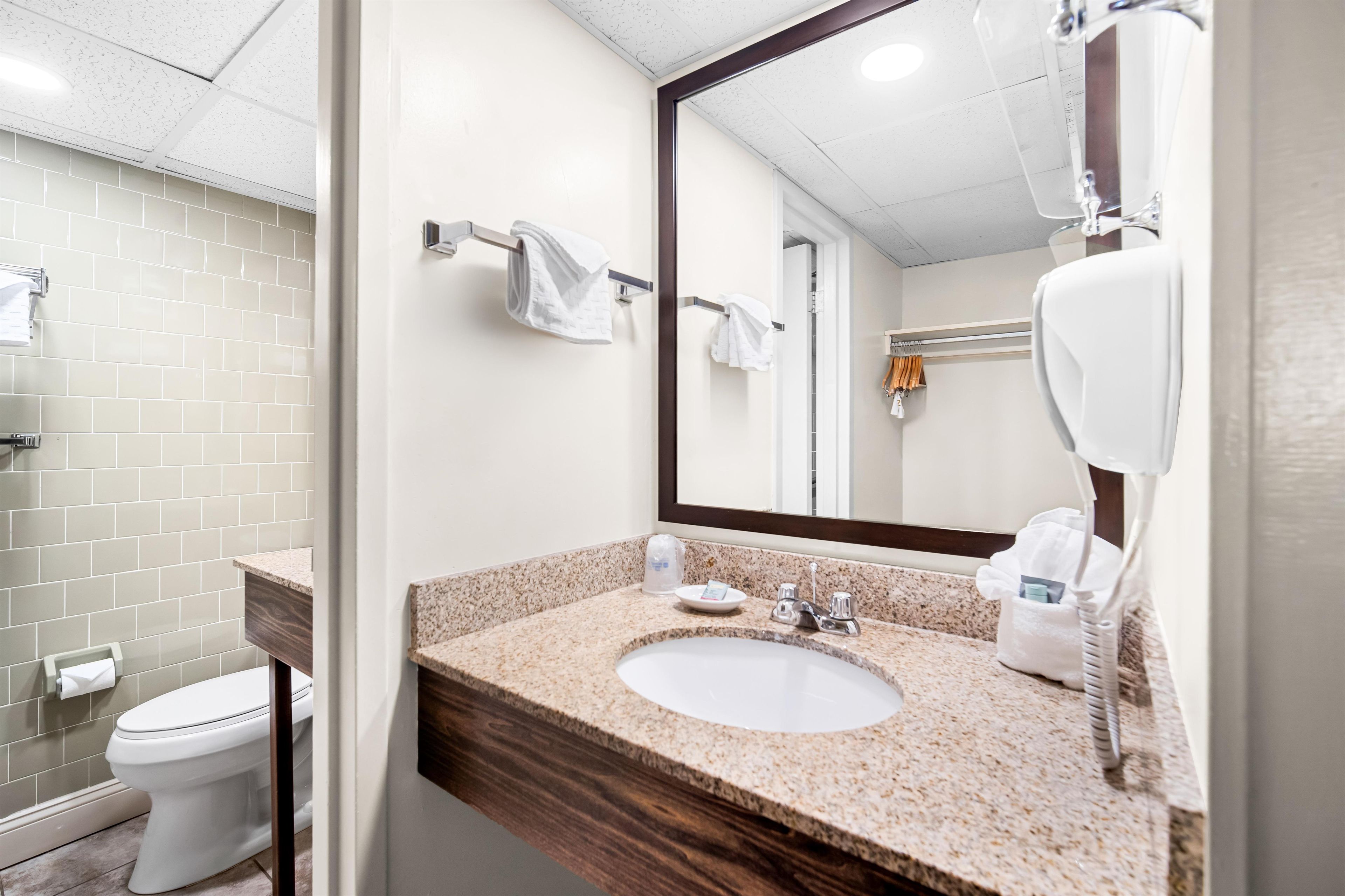 A modern bathroom with a white toilet, a granite countertop sink, a large mirror, and a towel rack.