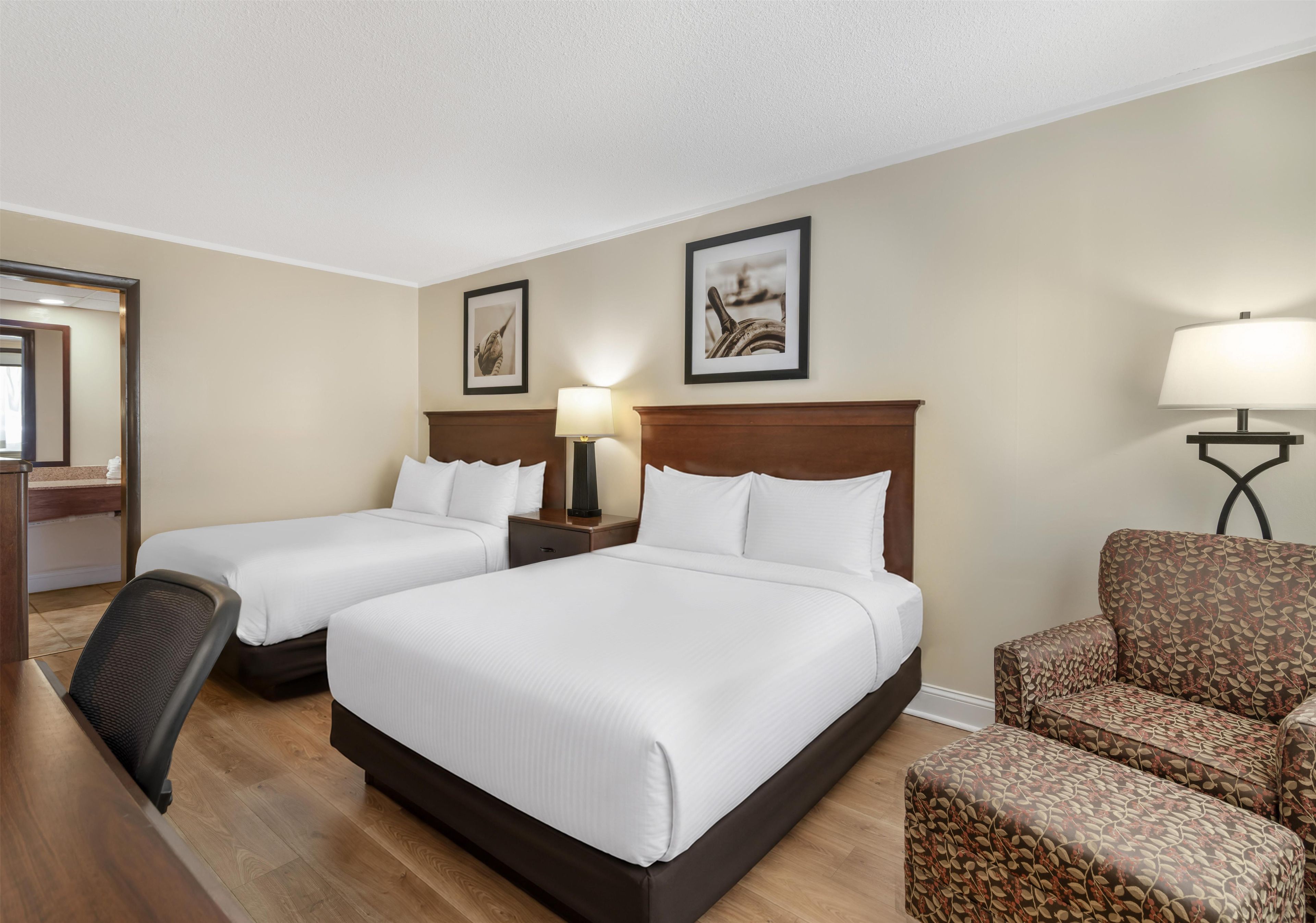 A hotel room with two beds, a desk, a chair, and two lamps.
