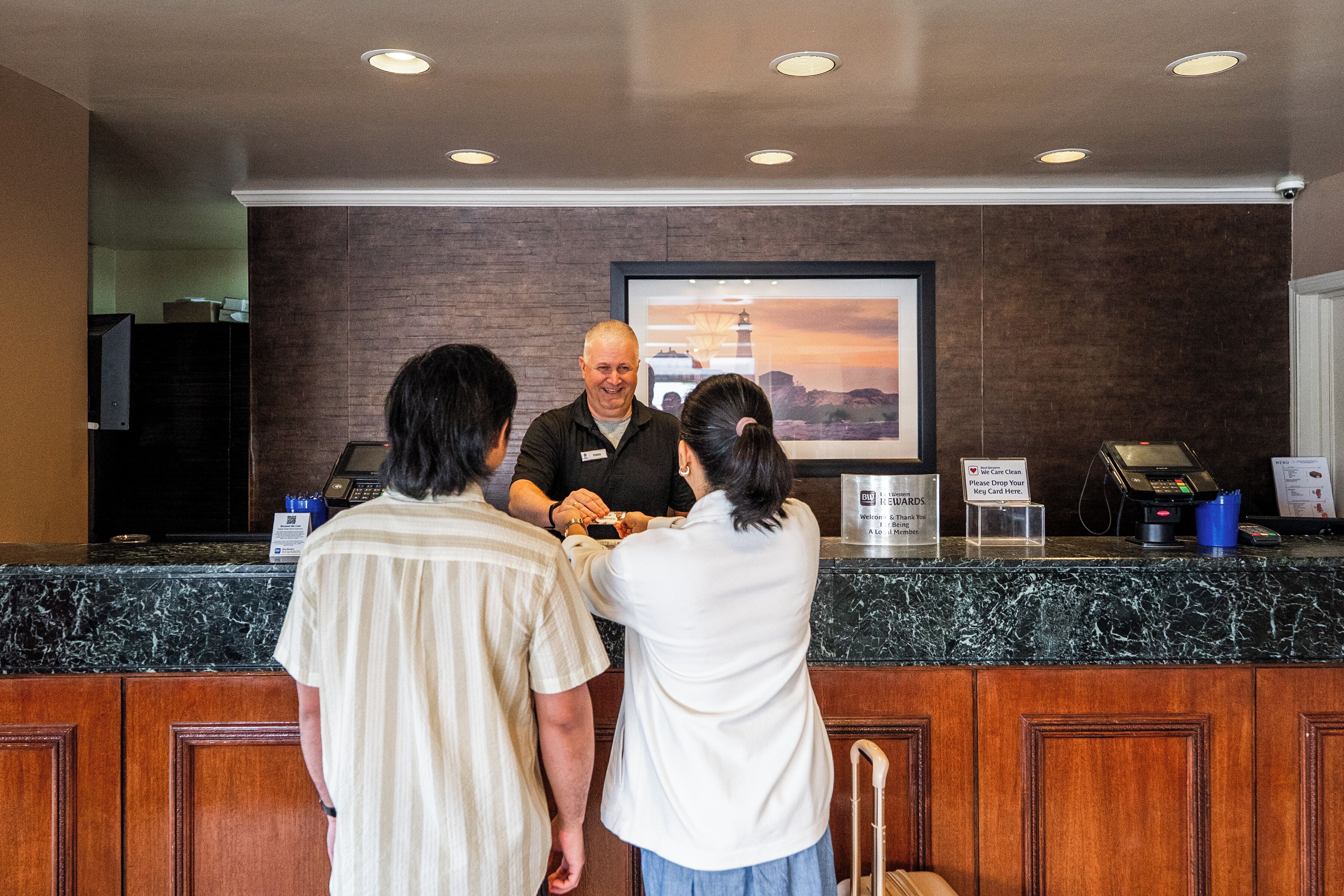 A reception desk with a marble counter, a framed picture of a sunset, and a sign instructing to drop off credit cards.