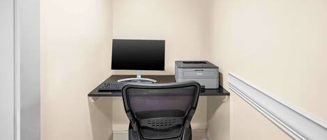 Un pequeño espacio de oficina con un escritorio, un monitor de computadora, una impresora y una silla.