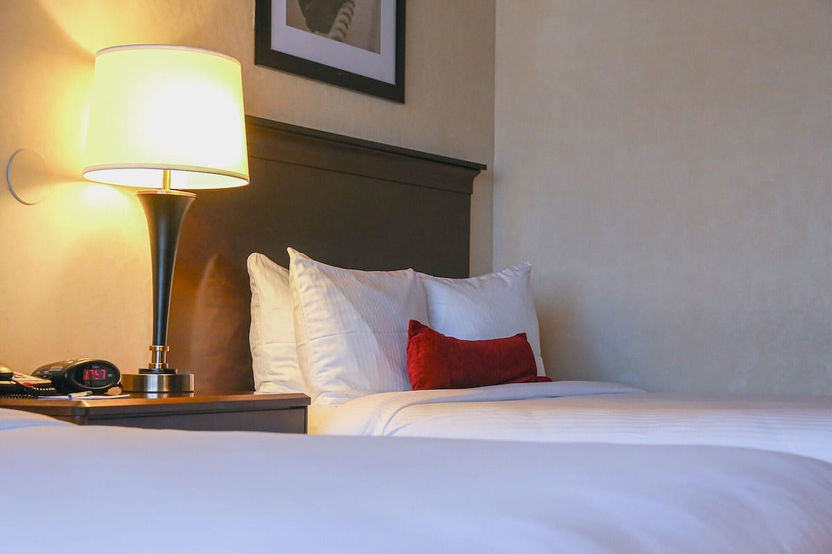 A neatly made bed with white and red pillows, a bedside lamp, and a clock on the nightstand.