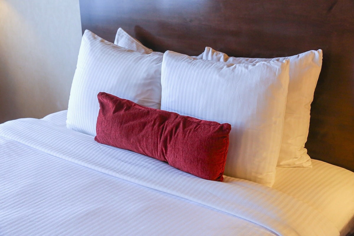 A bed with white bedding and a single red pillow.