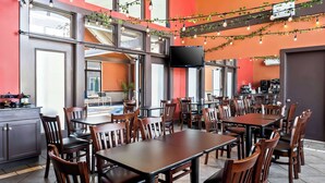 Un restaurant doté de nombreuses tables et chaises, de grandes fenêtres et d’un téléviseur à écran plat fixé au mur.