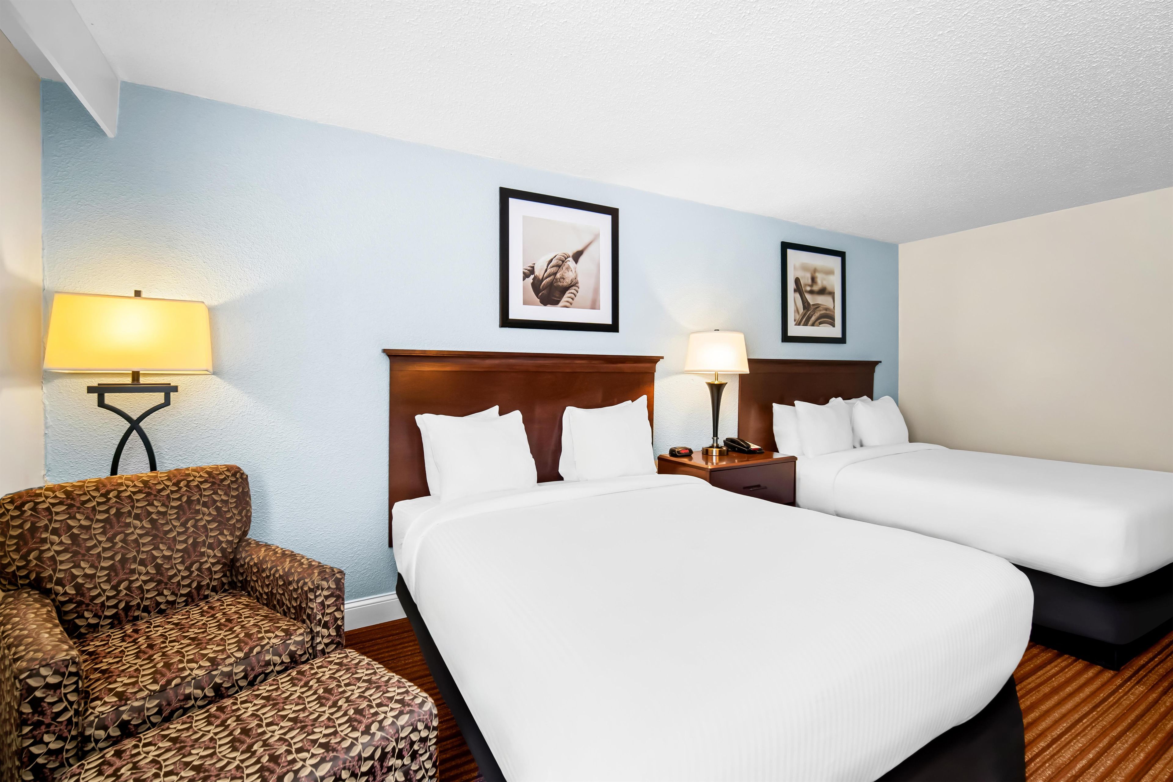A hotel room with two beds, a chair, and two wall-mounted lamps.