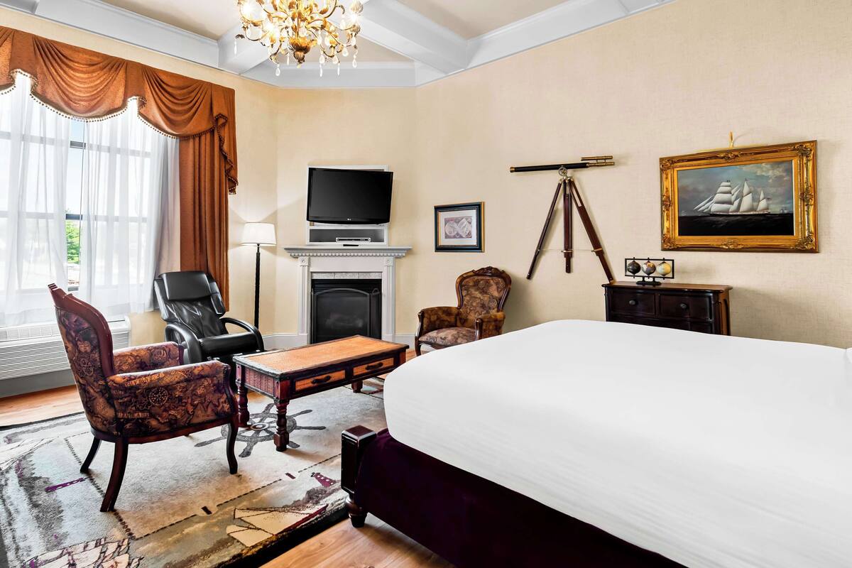 A hotel room with a large bed, a television, a fireplace, a desk, and a chair.