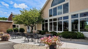 Un espace extérieur aménagé avec des tables et des chaises, un grand bâtiment aux grandes fenêtres et un arbre.