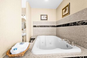 A modern bathroom with a large bathtub, a small sink, and a wicker basket with towels.