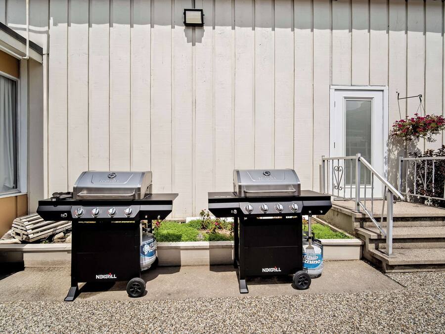 To NEXGRILL gasgrill placeret på en beton terrasse foran en bygning med hvide facader og en dør.