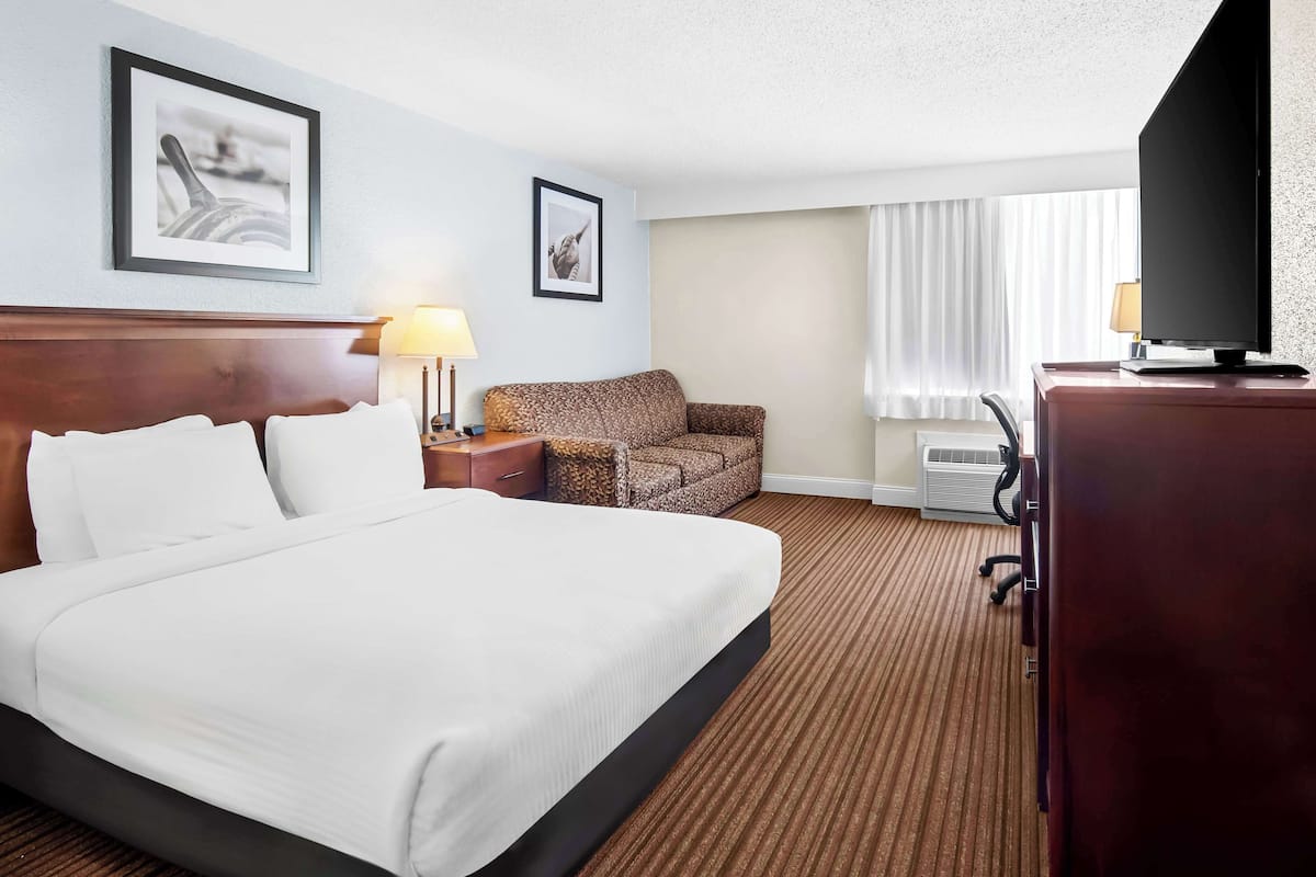 A hotel room with a large bed, a chair, a desk, a television, and framed pictures on the wall.