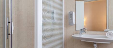 Un baño con cabina de ducha de vidrio, un lavabo blanco con espejo y una toalla sobre el lavabo.