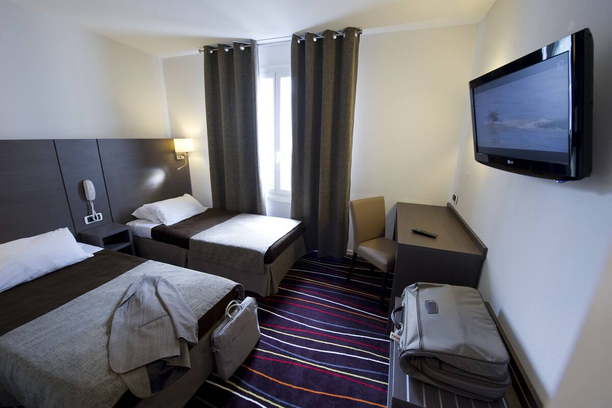 Habitación de hotel con dos camas, un escritorio, una silla, un televisor y una maleta.