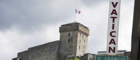 A historic stone building with a flag on top, a sign for "ASTORIA VATICAN" and "S' FRANCIS SHOP".