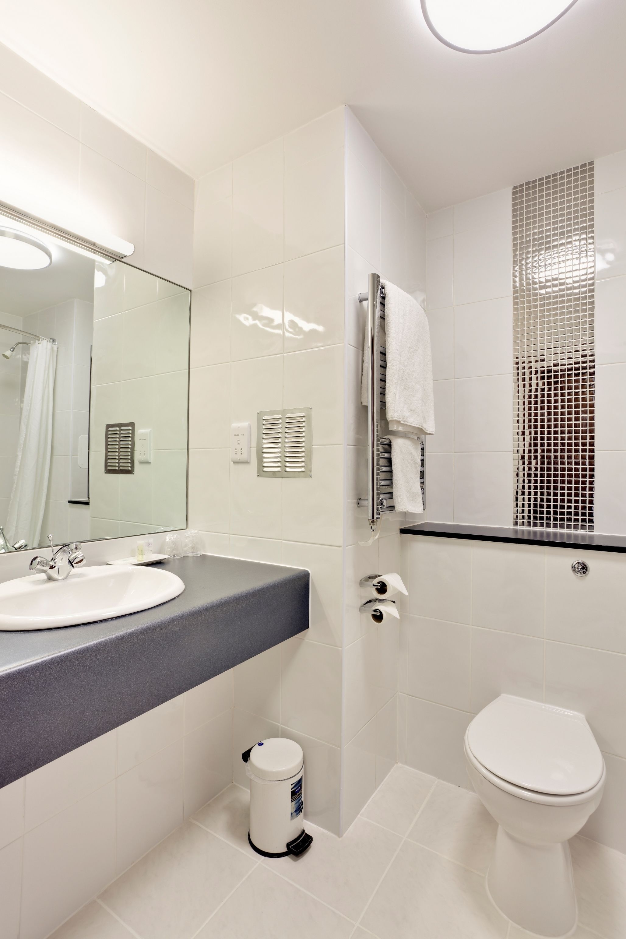 A modern bathroom with a white sink, mirror, and toilet.