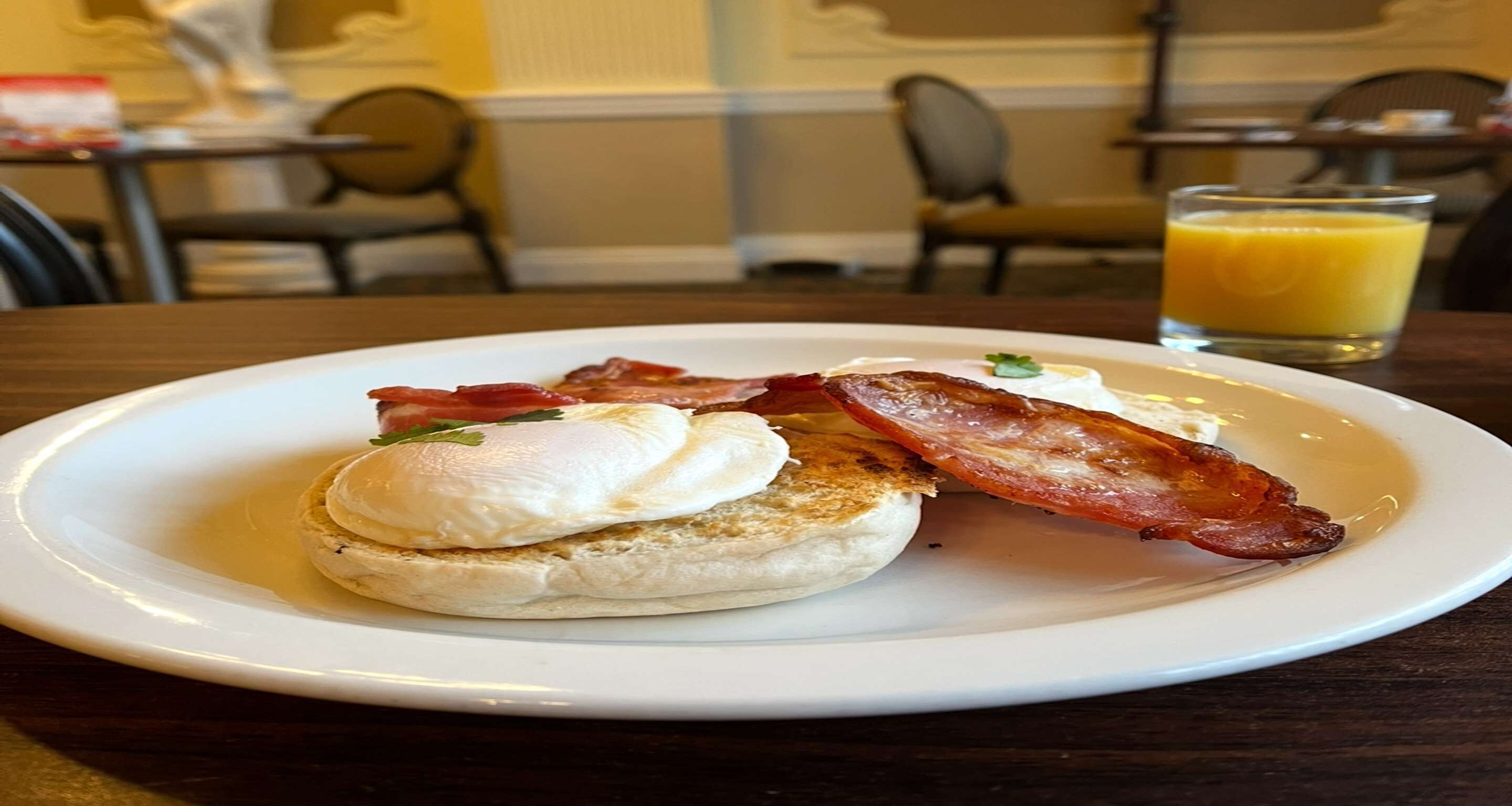 A breakfast plate with eggs, bacon, and a glass of orange juice on a table.