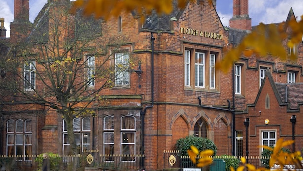 Un edificio tradicional de ladrillo con ventanas de arco y un letrero que dice "Plough & Harrow".