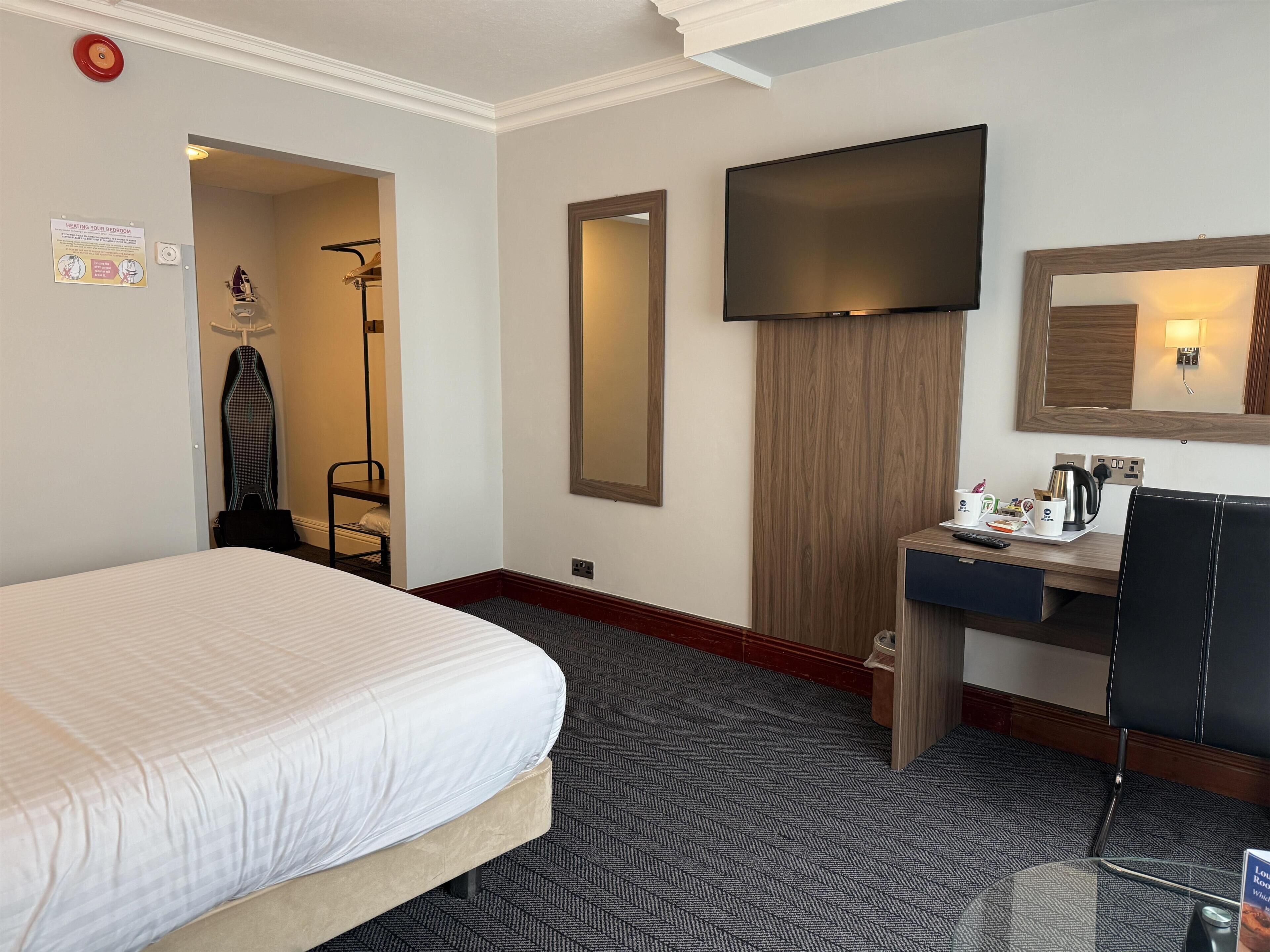 A hotel room with a bed, a desk with a chair, a TV, and a mirror.