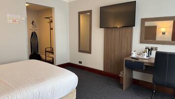 A hotel room with a bed, a desk with a chair, a TV, and a mirror.