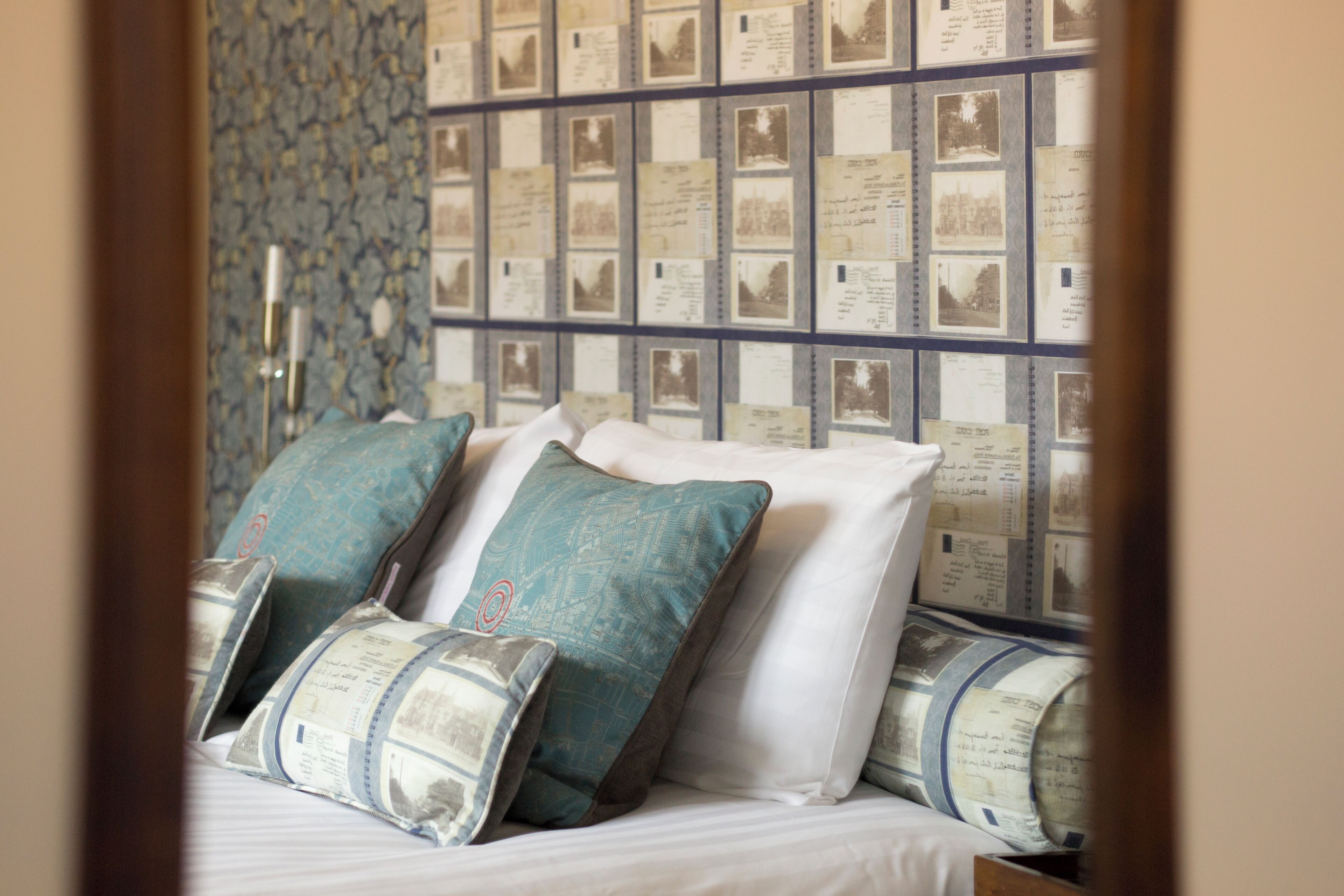 A neatly made bed with patterned pillows and a wall of framed photographs behind it.
