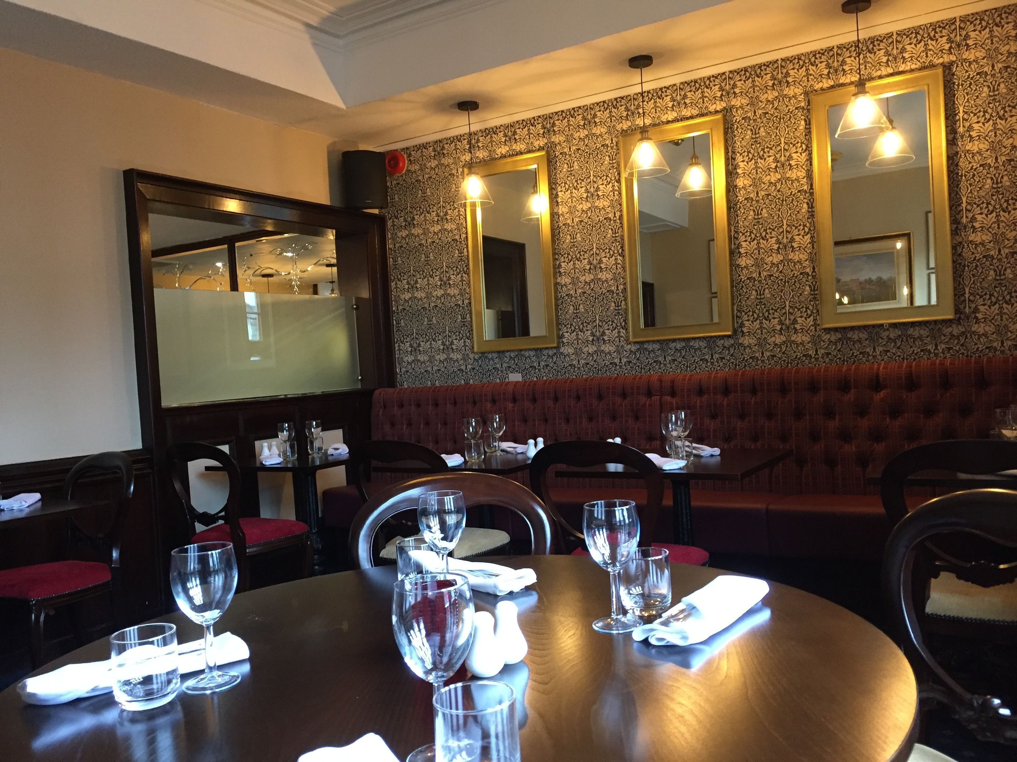 A restaurant with a wooden table set for dining, a red cushioned bench, and multiple mirrors on the wall.