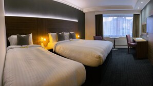 Una habitación de hotel con dos camas, un escritorio, una silla y una ventana con cortinas.