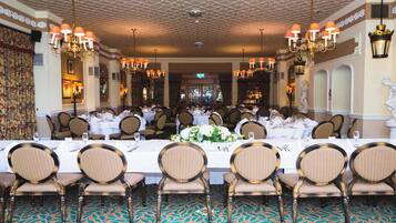 Een formele eetzaal met een lange tafel, gestreepte stoelen, kroonluchters en klassieke beelden.