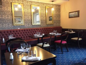 A restaurant with a red upholstered bench seating area, multiple tables with chairs, and wall-mounted mirrors. - Best Western Plough & Harrow Hotel (Birmingham)