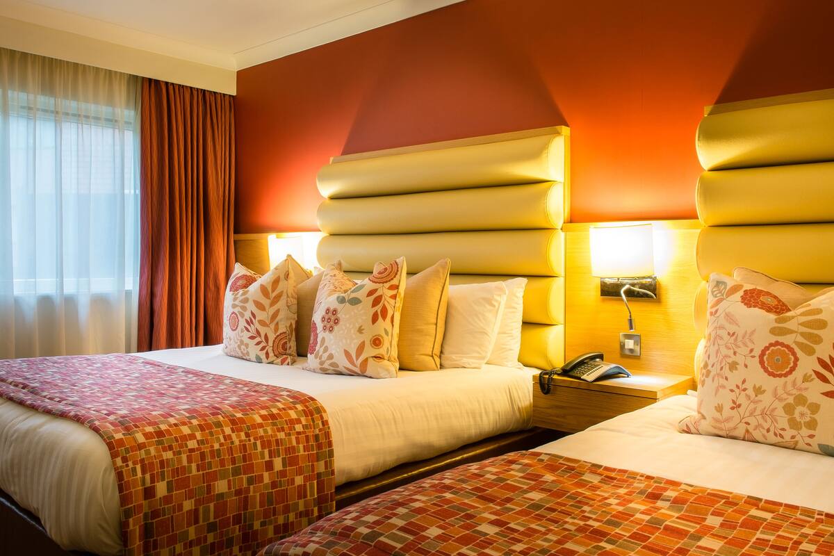 Une chambre d’hôtel avec deux lits, une table de chevet avec un téléphone et une fenêtre avec des rideaux.