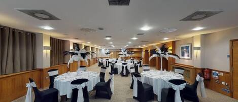A hotel conference room with round tables, black and white chairs, and decorative feather arrangements.
