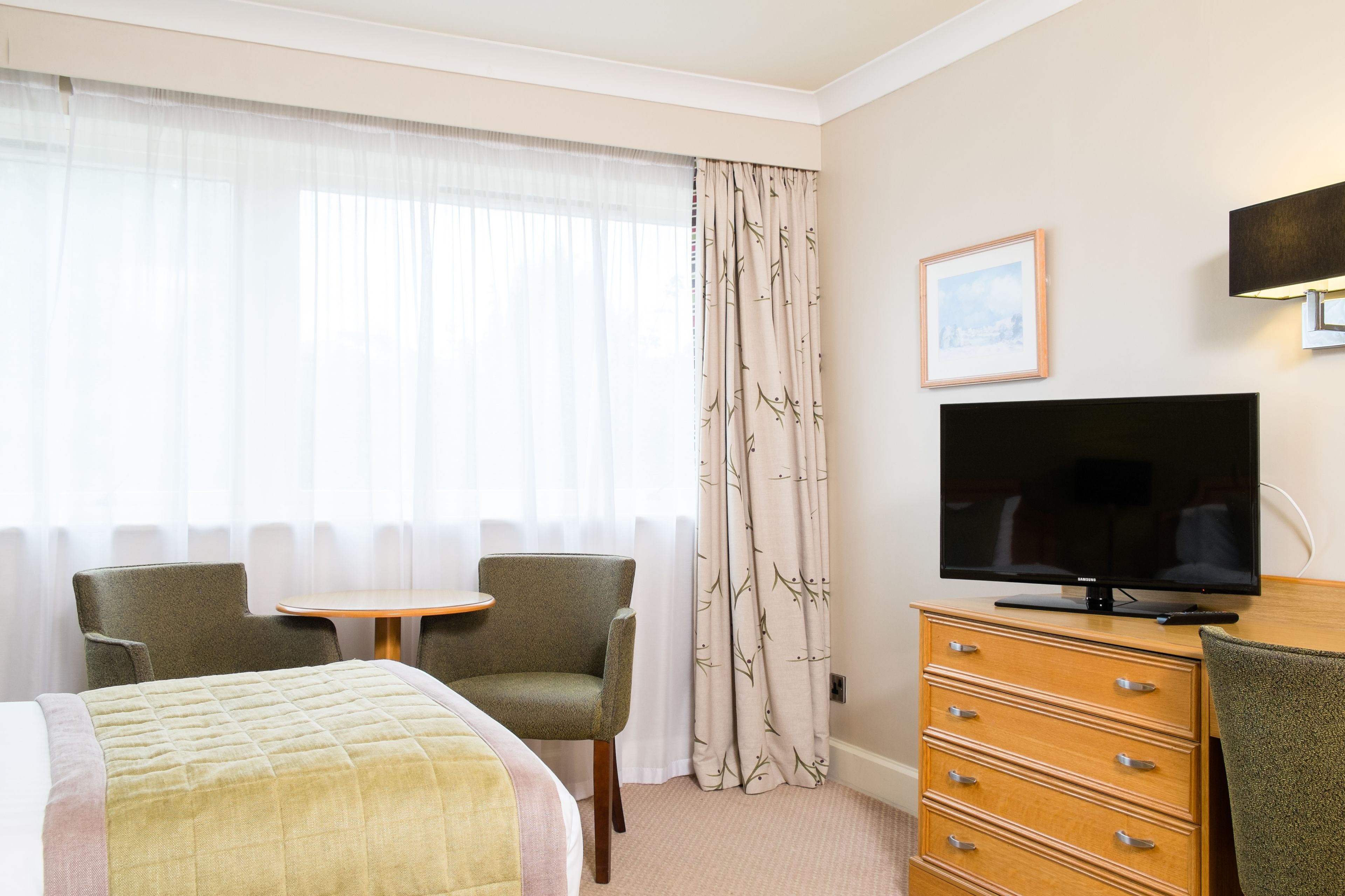 Ein Hotelzimmer mit einem Bett, zwei Stühlen, einem kleinen Tisch, einem Fernseher und einem Schminktisch.