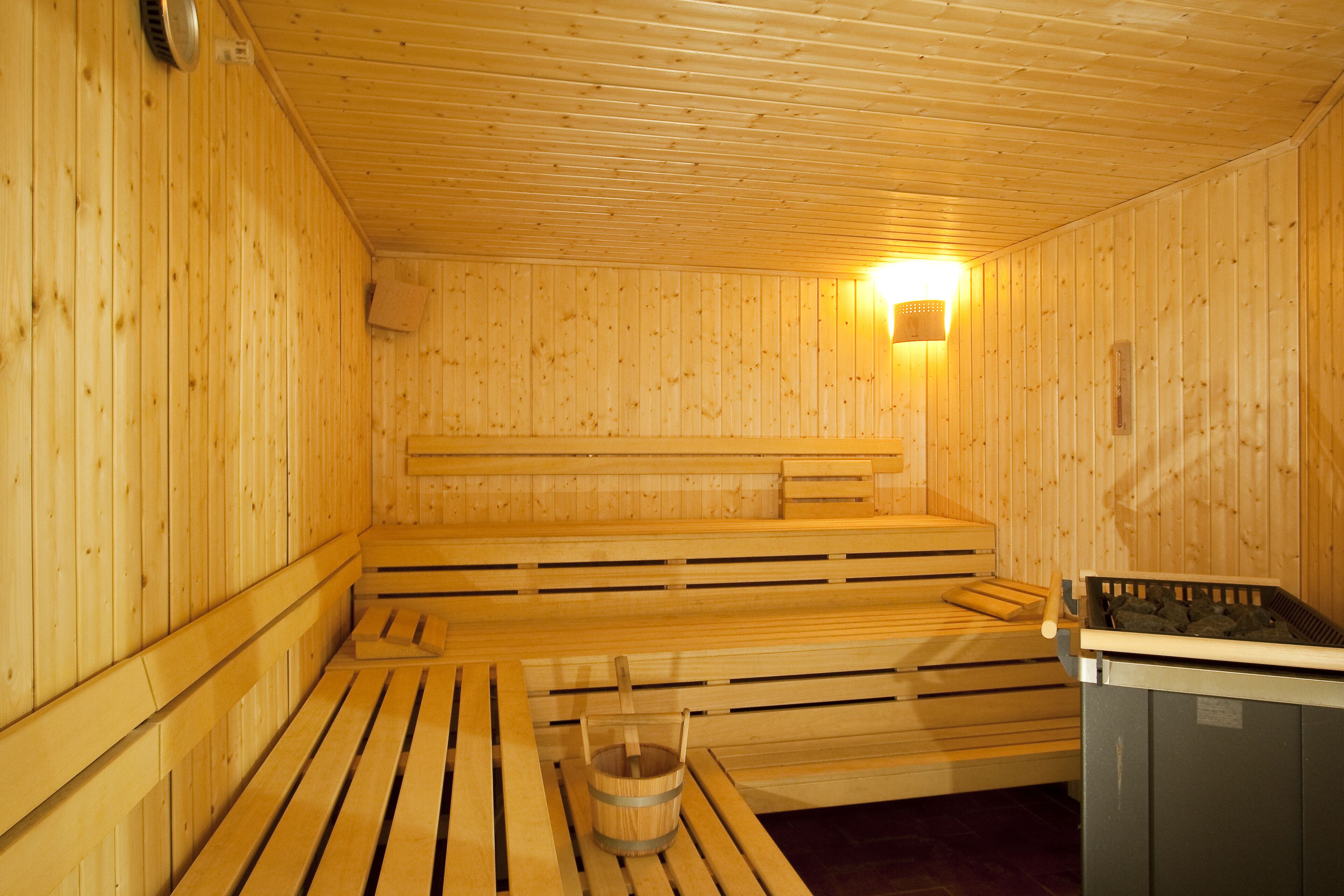 A wooden sauna with benches and a bucket of stones.