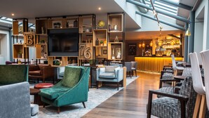 A spacious lounge area with a high ceiling, a bar in the background, and a variety of seating options including armchairs and sofas. - Lea Marston Hotel (Sutton Coldfield)