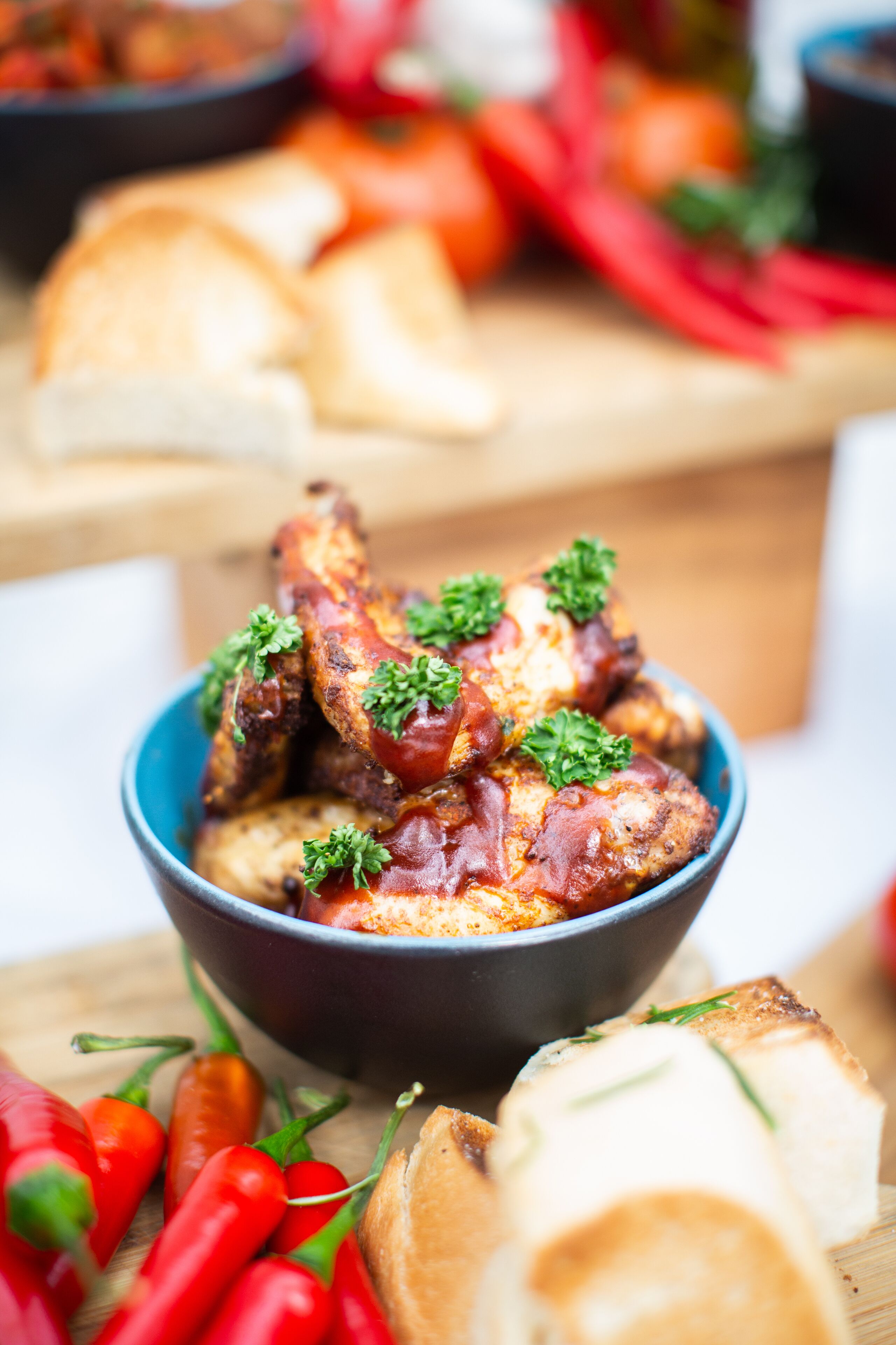 A bowl of chicken wings garnished with parsley, surrounded by bread and red chili peppers.